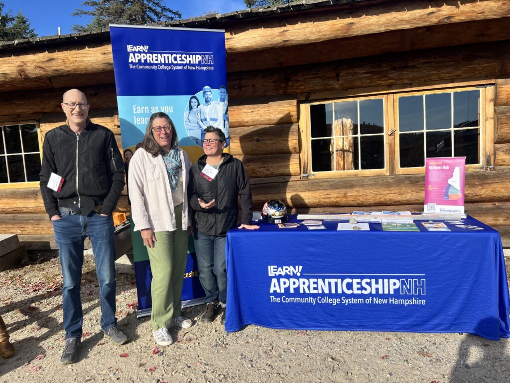 Three representatives from Apprenticeship NH are smiling in front of their table.