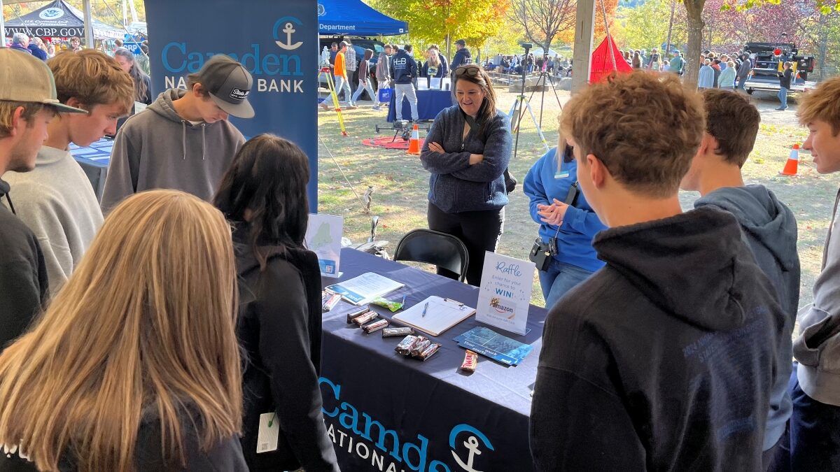 A representative from a bank is talking to students gathered around her table.