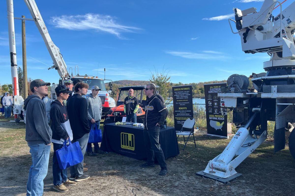 Students standing outside talking to representatives of an electric construction company.