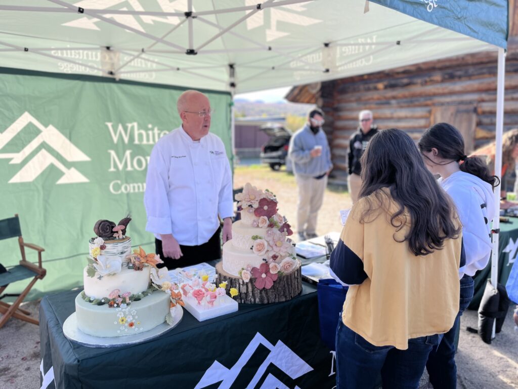 A representative from White Mountains Community College talking to students about the cake displays.